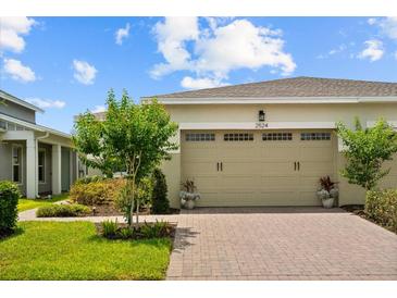 Beige two-car garage door with brick paver driveway and manicured landscaping enhance the curb appeal of this lovely home at 2524 Datura Loop, St Cloud, FL 34772