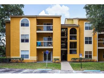 A yellow two story condo building with stairwells and lush trees on a bright day at 5267 Images Cir # 102, Kissimmee, FL 34746