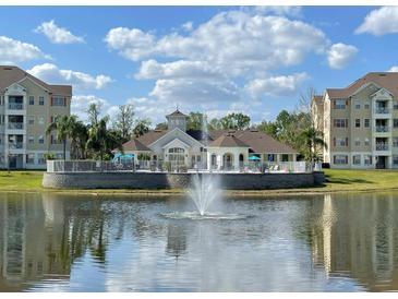 Beautiful clubhouse overlooking the lake with a fountain and palm trees against a blue sky at 5276 Cane Island Loop # 302, Kissimmee, FL 34746