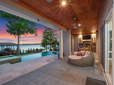Covered patio boasts an outdoor kitchen and cozy seating area next to a sparkling pool and serene lake view at 9916 Lone Tree Ln, Orlando, FL 32836