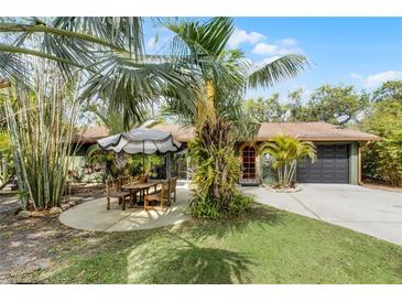 Charming single-story home featuring a lush, tropical landscaped yard and patio area with stylish umbrella at 1200 Auger Dr, New Smyrna Beach, FL 32168