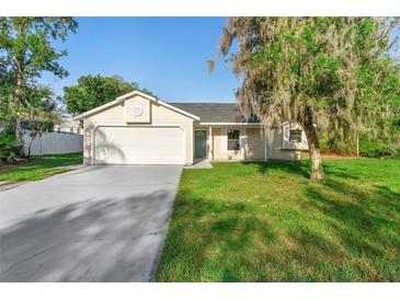 Charming single-Gathering home with an attached garage, light beige siding and well-manicured lawn and mature tree at 1550 Maxwell Ln, Deltona, FL 32738
