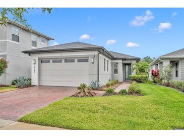 Charming single-Gathering home featuring a well-manicured lawn, gray paint, brick driveway, and two-car garage at 3149 Songbird Cir, Harmony, FL 34773