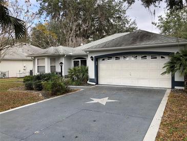 Charming single-story home with a gray driveway, a two-car garage, and landscaped front yard at 144 Costa Mesa Dr, Lady Lake, FL 32159