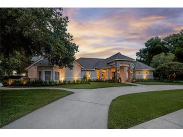 Stunning exterior of home with stone entryway, lush landscaping and circular driveway at sunset at 5025 Down Point Ln, Windermere, FL 34786