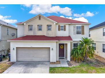 Charming two-story home featuring a red roof, two-car garage, and a beautifully landscaped front yard under a bright sky at 1744 Pine Ridge Dr, Davenport, FL 33896