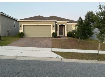 Charming single-story home featuring a two-car garage, brick driveway, and manicured landscaping at 176 Jensen Dr, Groveland, FL 34736