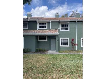 Exterior shot of a green two-story townhouse with a red tile roof, windows, and landscaping at 4503 Oak Arbor Cir, Orlando, FL 32808
