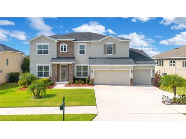 Charming two-story home with a three-car garage and stone accents, set against a backdrop of lush landscaping and a bright blue sky at 16410 Good Hearth Blvd, Clermont, FL 34711