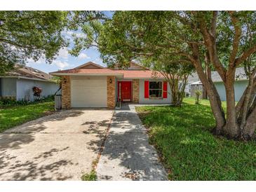 Charming single-story home featuring brick accents, a red front door, and mature trees in a well-maintained yard at 916 Glendale St, Orlando, FL 32807