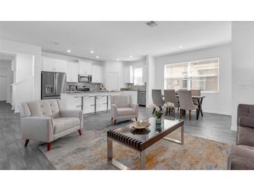 Bright, open-concept living room with modern furnishings, adjacent to a kitchen with stainless steel appliances at 6328 Whip O Will Ln, St Cloud, FL 34771