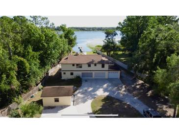 Aerial view of a beige two-story home with a three-car garage and a nearby private dock on the lake at 4981 Lake Cecile Dr, Kissimmee, FL 34746