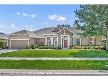 Charming single-story home with manicured lawn, stone accents, red door, and lush landscaping at 369 Torgiano Dr, Ocoee, FL 34761