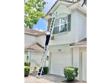 Exterior view of home's facade, featuring a tile roof, two-car garage, and landscapers on ladders doing exterior work at 7054 Cadiz Blvd, Orlando, FL 32819