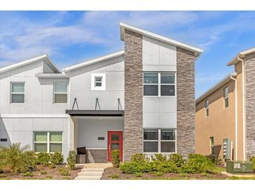Modern two-story home featuring a stone facade, gray siding, and a vibrant red front door at 4375 Scene Ln, Kissimmee, FL 34746