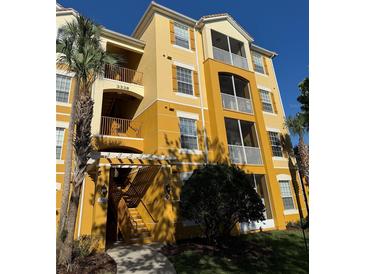 Condo building with yellow facade, wood shutters, multiple balconies, and lush green landscaping at 3338 Robert Trent Jones Dr # 30704, Orlando, FL 32835