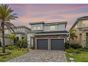 Two-story home featuring stone accents, a brick driveway, lush landscaping, and a two-car garage at 15702 Vetta Dr, Bella Collina, FL 34756