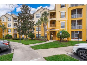 Three-story condo building featuring balconies, vibrant yellow paint, and lush landscaping at 3338 Robert Trent Jones Dr # 203, Orlando, FL 32835