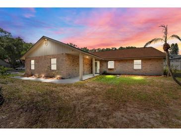 Charming single-story brick home featuring a well-maintained lawn and mature trees under a beautiful sunset sky at 10545 Parkway Dr, Clermont, FL 34711