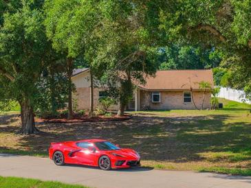 Quaint single-story brick home nestled among mature trees with a red Corvette parked out front at 10545 Parkway Dr, Clermont, FL 34711