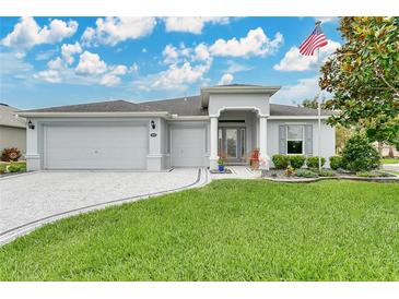 Inviting single-story home featuring a well-manicured lawn, three-car garage, and a charming American flag at 4002 Richmond Xing, Leesburg, FL 34748