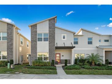 Modern two-story home with stone accents, manicured landscaping, and a vibrant red front door at 1128 Challenge Dr, Davenport, FL 33896