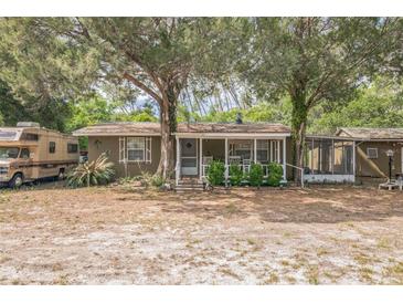 Charming single-story home featuring a cozy front porch nestled among mature trees and landscaping at 24089 Ne 152Nd Ln, Fort Mc Coy, FL 32134