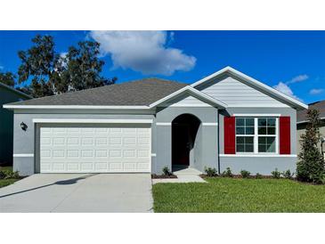 Charming single-story home with a two-car garage, gray stucco siding, red shutters, and a well-manicured lawn at 3418 Wynwood Forest Dr, Ocoee, FL 34761
