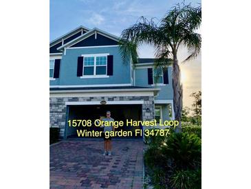 Two story home with light blue facade, brick driveway, and integrated two car garage and well landscaped front yard at 15708 Orange Harvest Loop, Winter Garden, FL 34787