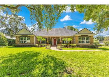 Charming brick home featuring manicured lawn, mature trees, and a welcoming red front door at 8812 S Bay Dr, Orlando, FL 32819