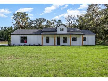 Charming single-story home featuring a modern farmhouse design with a large front yard and wooden porch columns at 13393 Sw 484 Hwy, Ocala, FL 34481