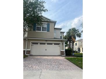 Two-story tan home with a large two-car garage and brick paver driveway at 1122 Priory Cir, Winter Garden, FL 34787