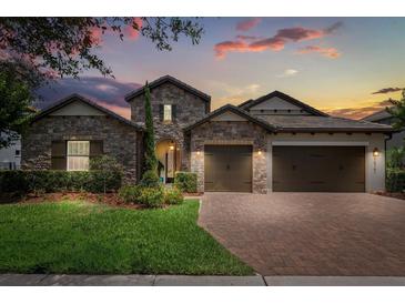 Charming stone home featuring a three-car garage, brick paver driveway and lush landscaping at 16761 Broadwater Ave, Winter Garden, FL 34787