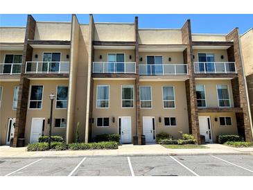 Modern townhome exterior with a glass balcony, lush landscaping and convenient parking spaces at 7667 Recife Dr, Kissimmee, FL 34747