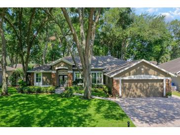 Beautiful single-story home featuring a lush, green lawn and a brick-accented facade with mature tree landscape at 920 Cool Springs Cir, Ocoee, FL 34761