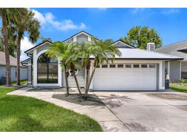 Charming single-story home featuring a two-car garage, arched window, gray paint, and decorative palm trees at 2391 Piedmont Lakes Blvd, Apopka, FL 32703