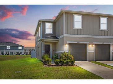 Charming two-story townhome featuring an attached garage, manicured lawn and inviting facade at sunset at 1401 Mirabella Cir, Davenport, FL 33897