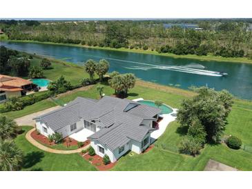 Stunning aerial view of a waterfront home with a pool and lush landscaping, featuring boaters enjoying the water at 12508 Lake Denise Blvd, Clermont, FL 34711