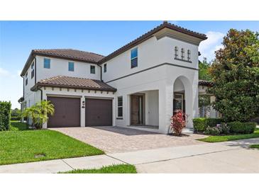 Two-story home with a two-car garage, white exterior, brown tile roof and a brick driveway, complemented by lush landscaping at 11707 Hampstead St, Windermere, FL 34786