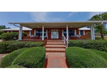 Charming brick home with inviting front porch, white columns, swings, and manicured landscaping at 4895 Cr 134B, Wildwood, FL 34785
