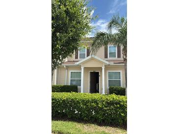 Inviting tan home featuring a covered porch, brown shutters, and manicured landscaping, perfect for comfortable living at 3229 Cupid Pl, Kissimmee, FL 34747