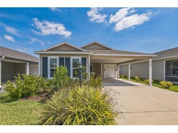 Charming single-story home with tan siding, blue shutters, and a well-manicured front yard and an attached covered carport at 747 Louise Ln, The Villages, FL 32163