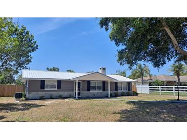 Charming home featuring a metal roof, stone accents, and mature trees in a well-manicured front yard at 11624 Ocklawaha Dr, Leesburg, FL 34788