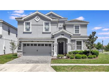 Charming two-story home with manicured lawn, gray facade, arched entryway, and a two car garage at 1533 Flange Dr, Davenport, FL 33896