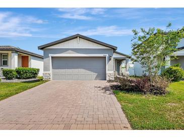 Charming single Gathering home featuring a gray stucco exterior, two-car garage and a brick paver driveway at 29400 Caspian St, Leesburg, FL 34748