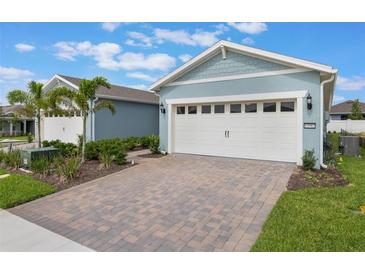 Light blue home exterior featuring a two-car garage with brick paver driveway and mature landscaping at 13562 Pearl Beach St, Winter Garden, FL 34787
