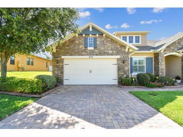 Charming stone home featuring a two-car garage with brick paver driveway and lush landscaping at 4133 Foxhound Dr, Clermont, FL 34711