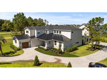 Beautiful modern home with a metal roof, brick driveway, manicured lawn, and lush, mature landscaping at 7706 Ficquette Rd, Windermere, FL 34786