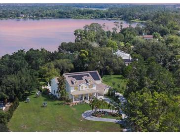 Stunning aerial view of a lakeside home with solar panels, mature trees, and a circular driveway at 5351 Carson St, St Cloud, FL 34771