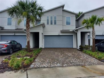 Attractive townhome featuring a two-car garage, modern design, palm trees, and brick paver driveway at 3316 Bellissimo Ave, Kissimmee, FL 34746